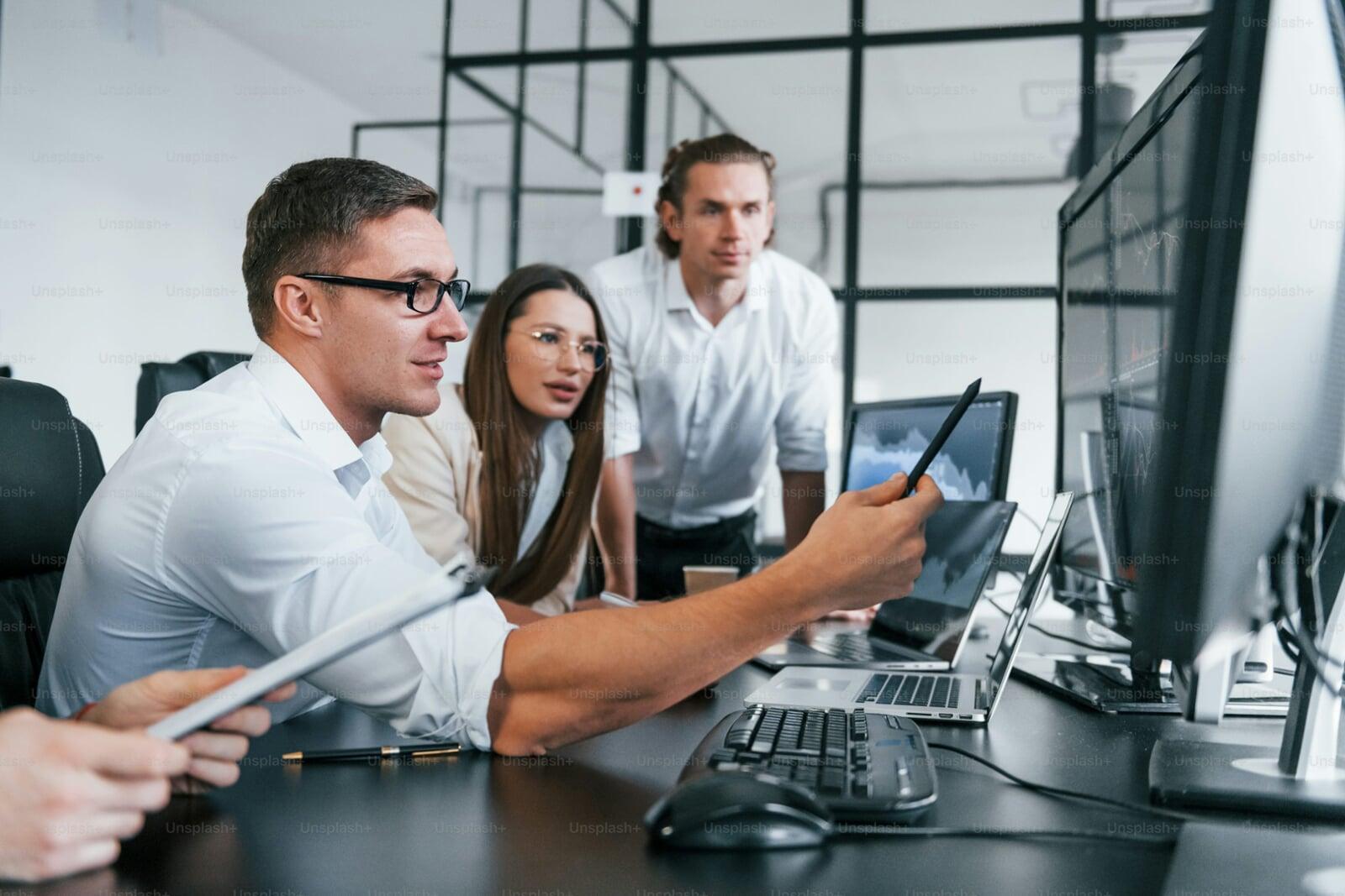 Team of professionals collaborating on CRM software implementation, reviewing data and strategies on multiple computer screens.